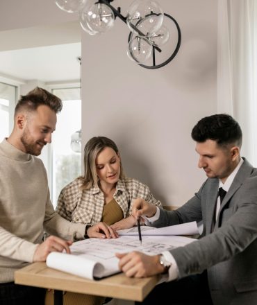 Couple discussing a blueprint with a real estate agent, planning their new home purchase.